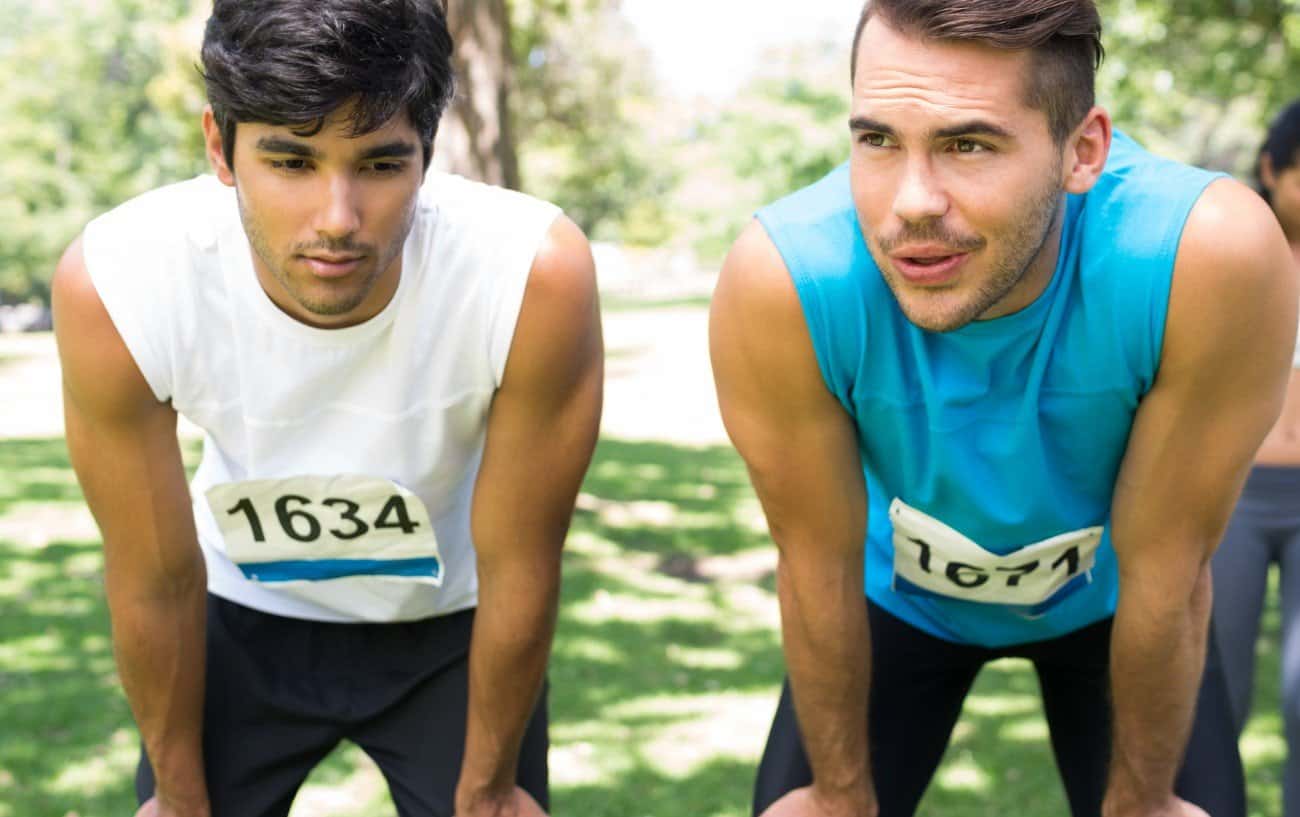 Two runners hunched over with their hands on their knees looking tired.