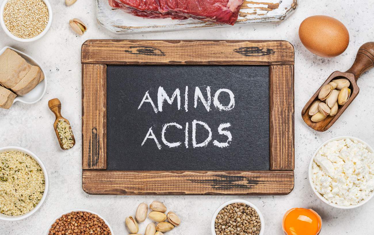 A small chalkboard with amino acids written on it surrounded by foods high in protein. 