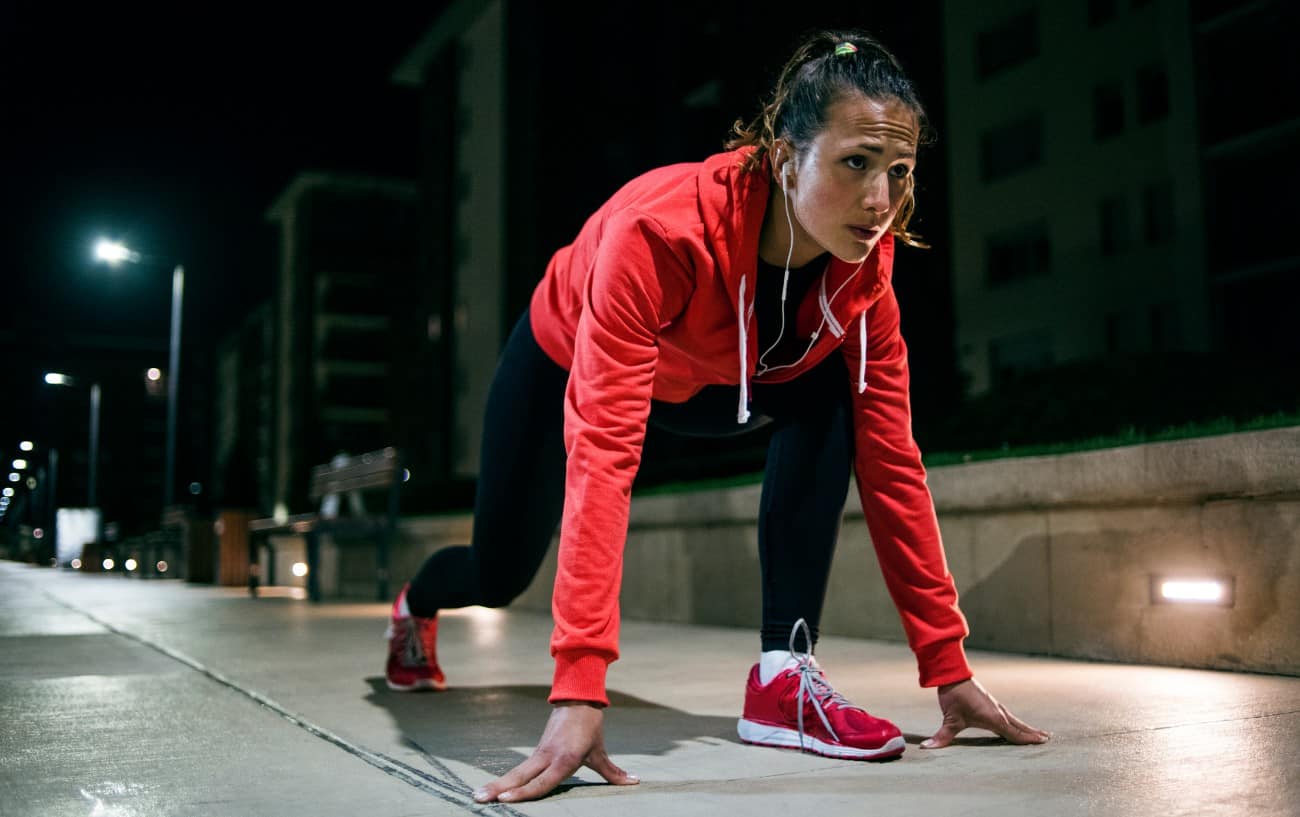 A woman outside in the evening getting ready to sprint. 