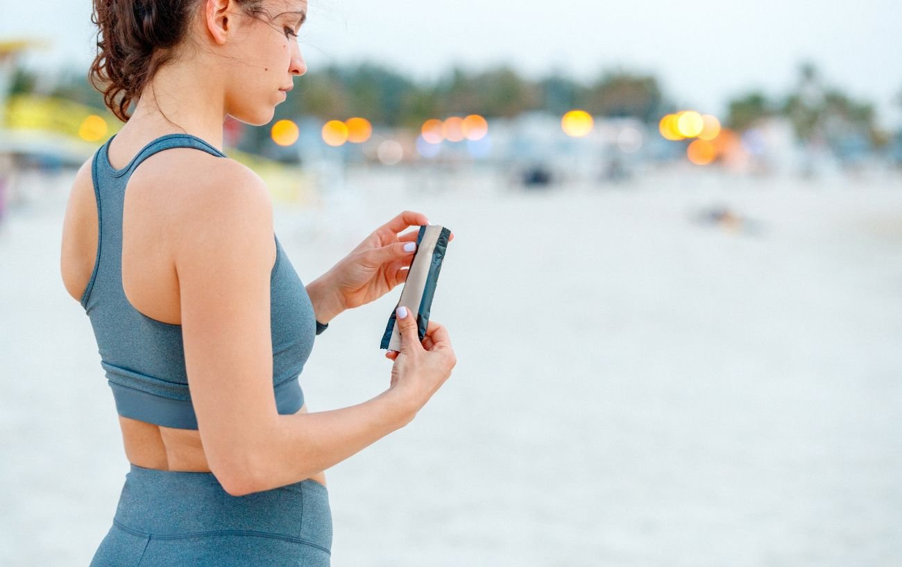 A person in workout clothes unwrapping a protein bar.