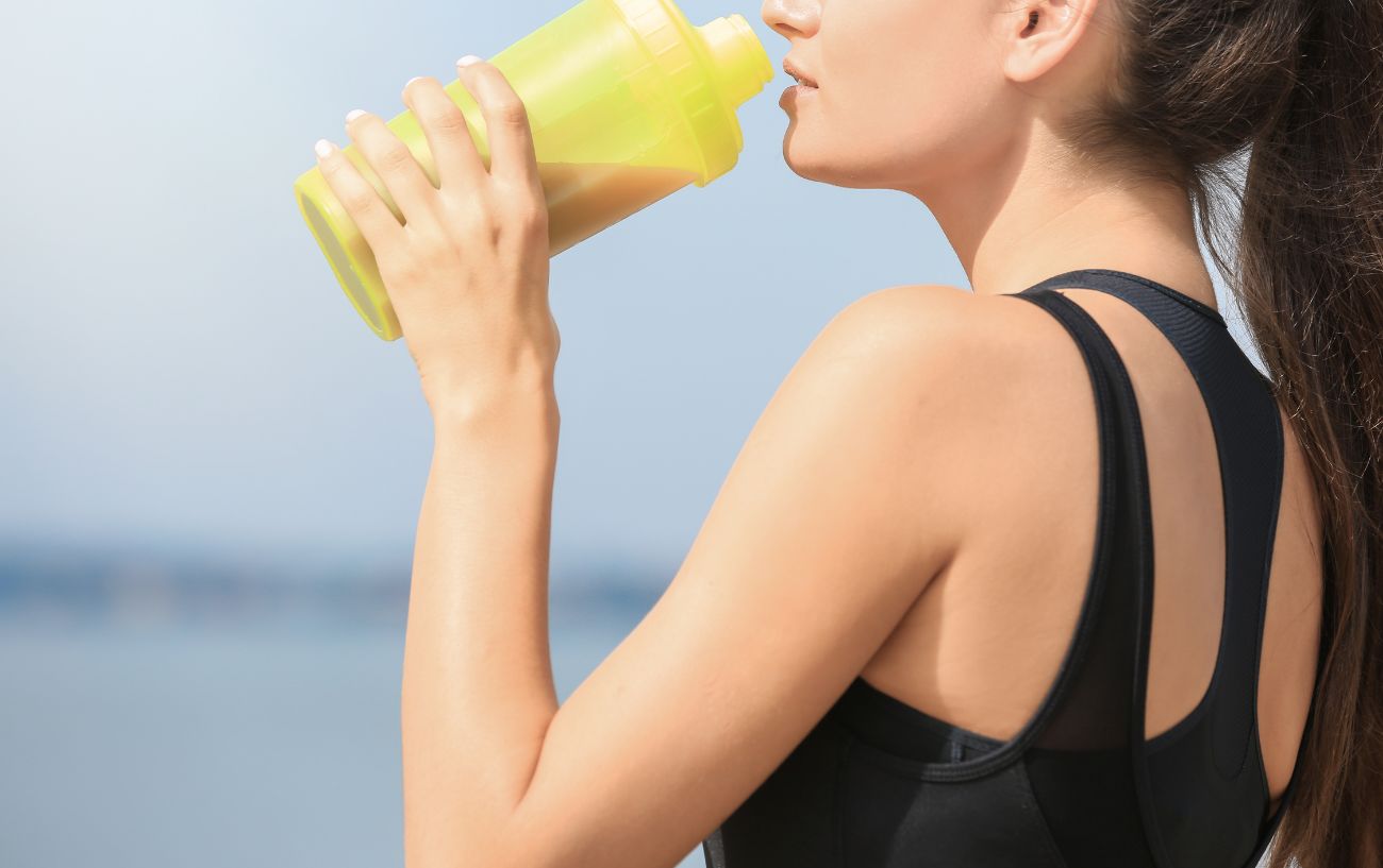 A person drinking from a yellow protein shaker.