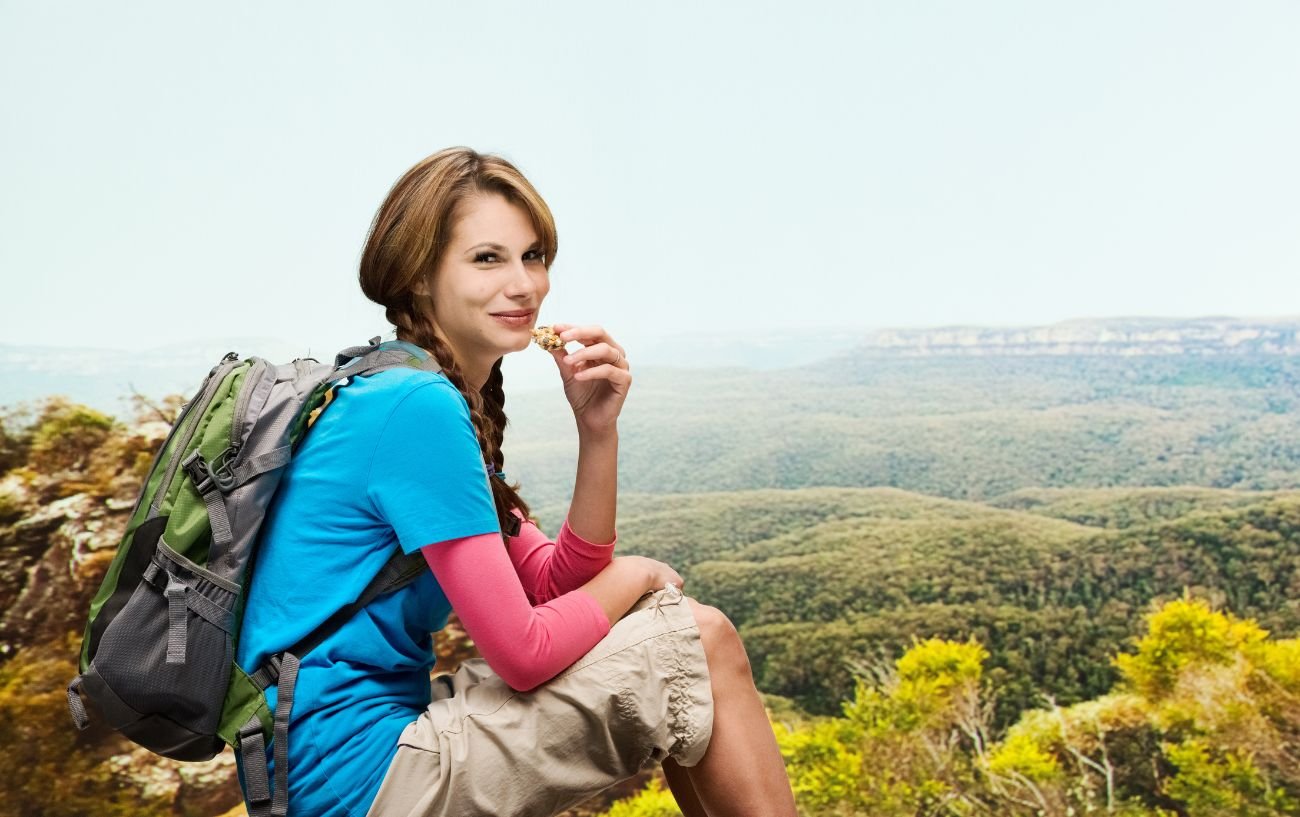 A hiker resting and eating a protein bar.