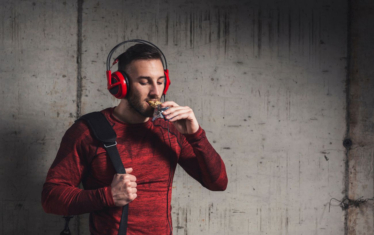 A person with red headphones biting into a protein bar.