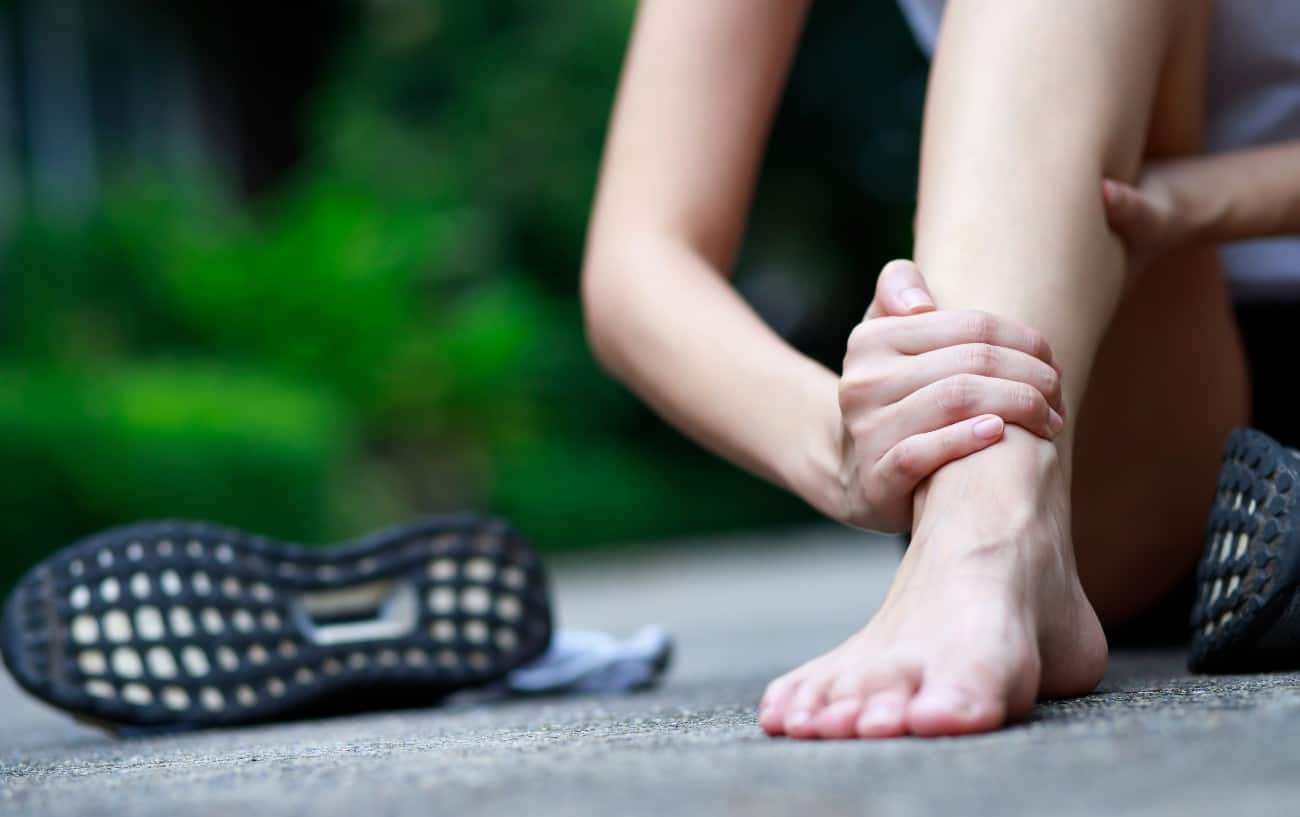 A person sits on the road barefoot holding their ankle.