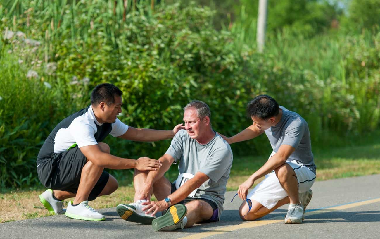 A man sits on the ground holding his ankle.