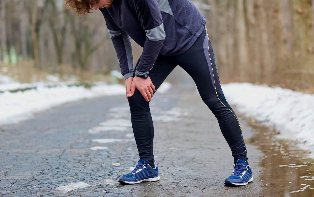 A runner stands on the road with their hands on their knee.