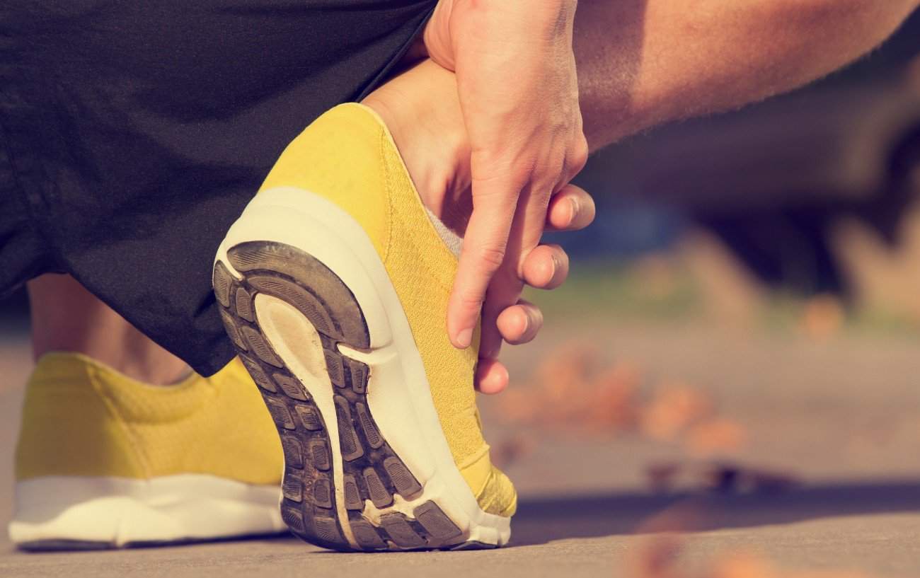 A person wearing yellow running shoes holds their ankle.