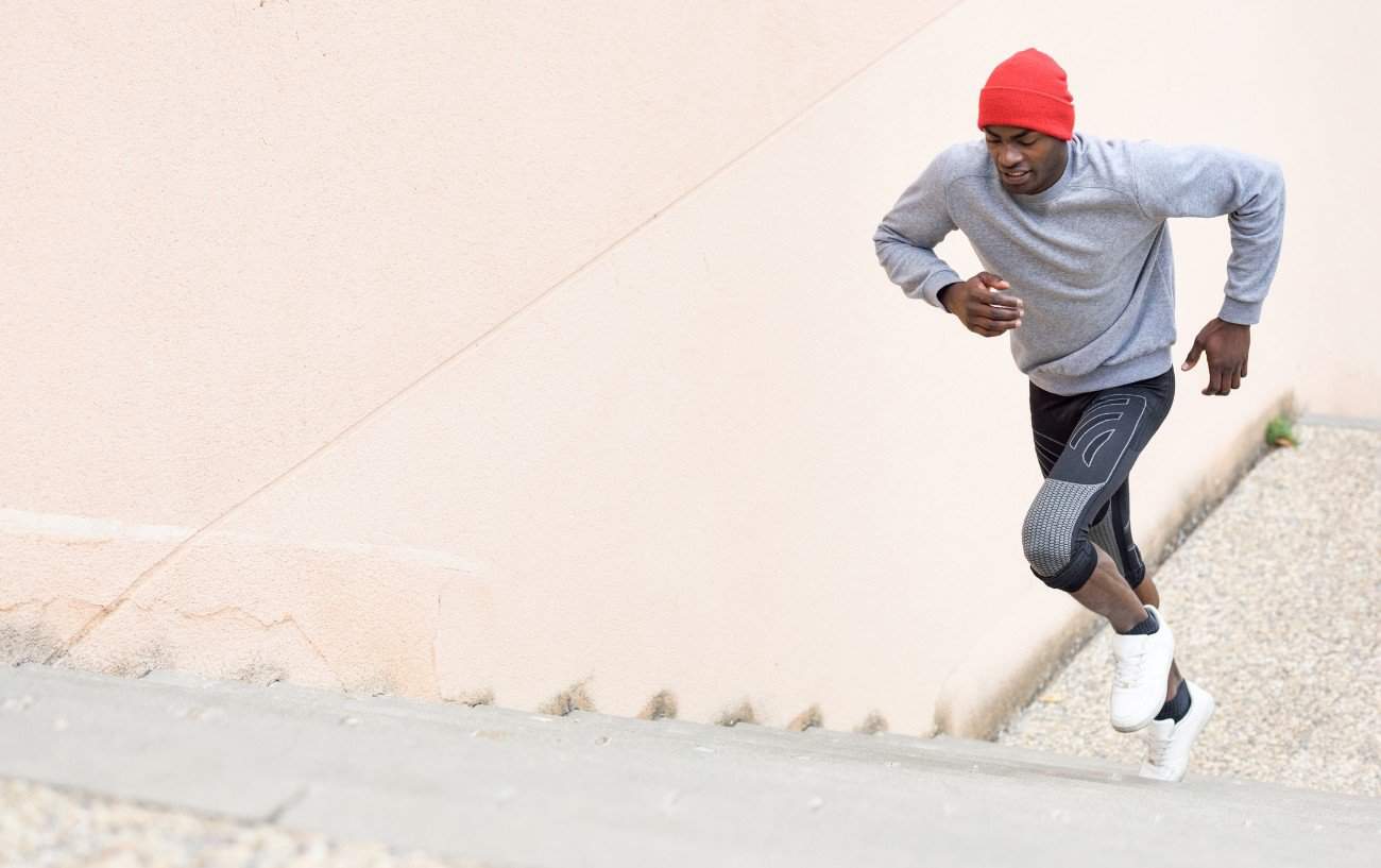 A runner wearing a red hat sprints up some stairs.