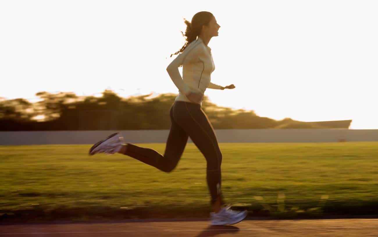 A woman runs around a track with the sun in the background.