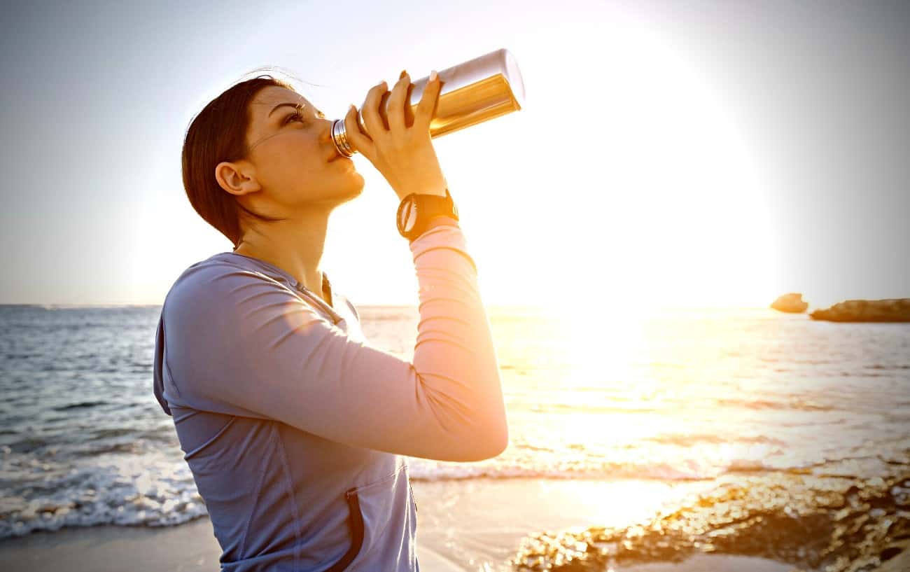 A person at the beach drinking from a bottle of water. 