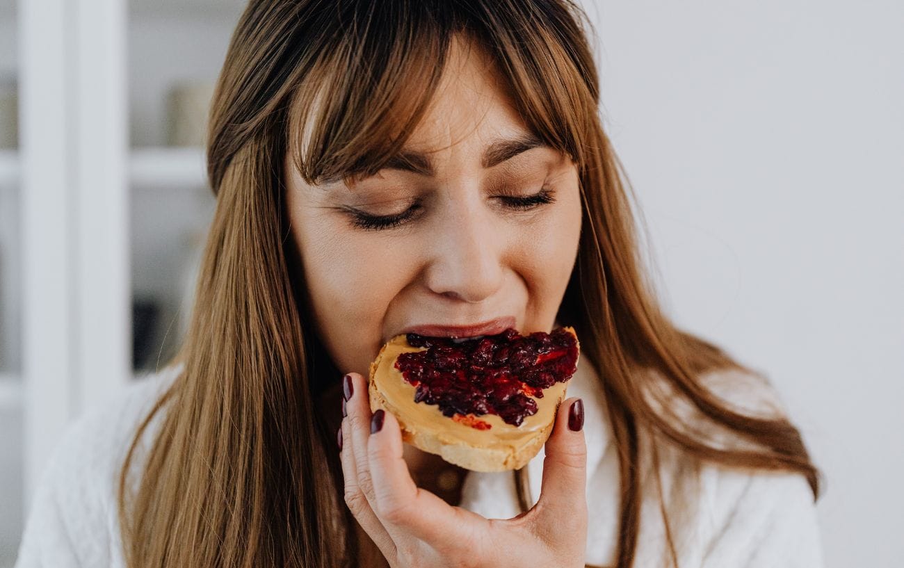 A woman eating toast with peanut butter and jelly.
