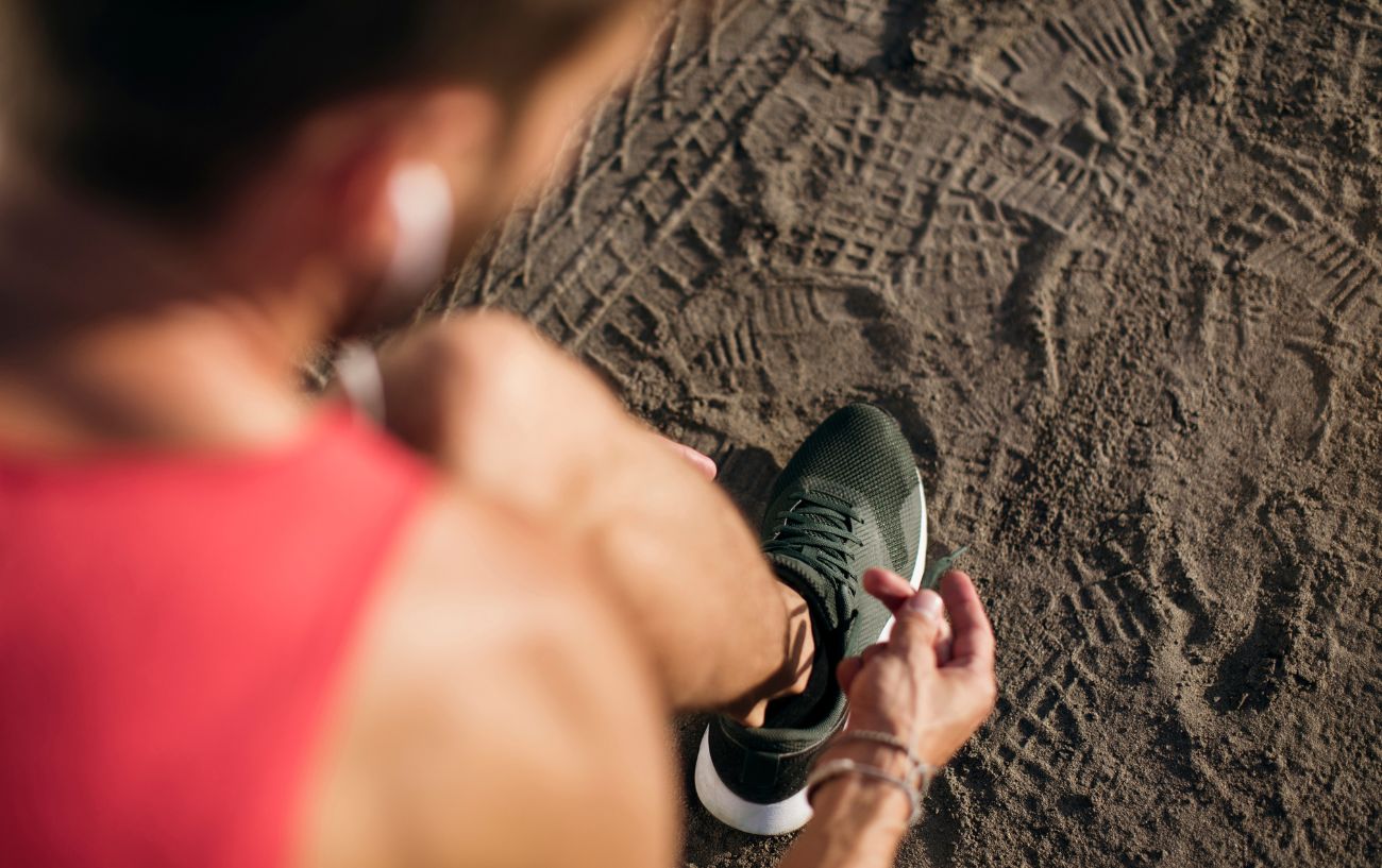 A person tying their running shoe in the dirt.