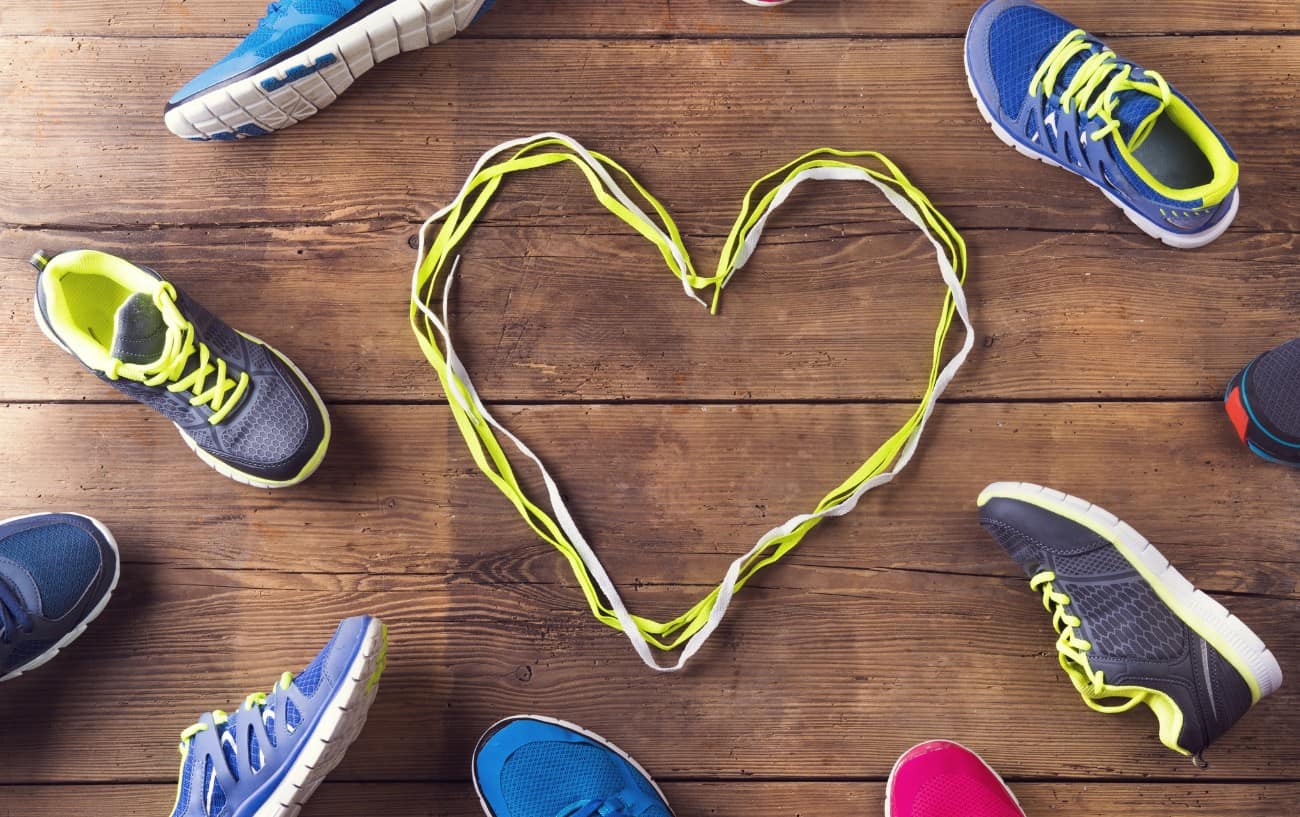A bunch of running shoes on the floor with a heart in laces in the middle. 